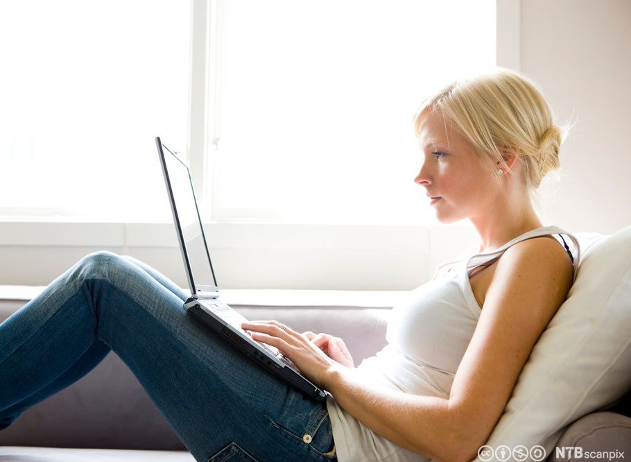 Ung kvinne med bærbar datamaskin i fanget. Foto.