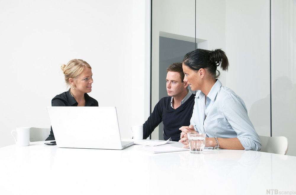 To kvinner og ein mann sit framfor ein PC og diskuterer. Foto.