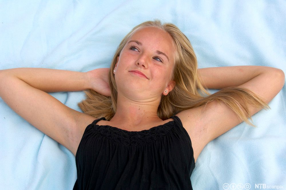 Ei jente som ligger med hendene bak hodet og ser ut i lufta med et svakt smil. Foto.