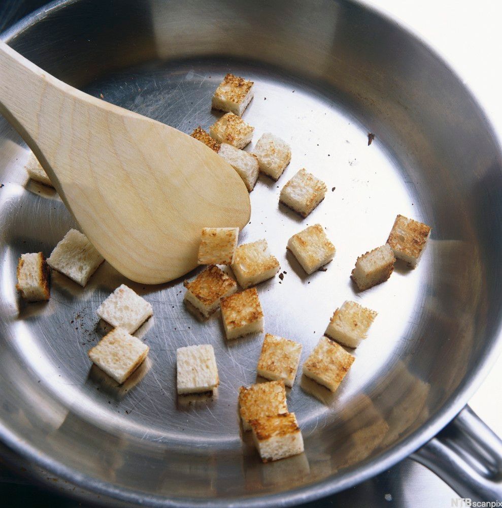 Brødkrutonger som stekes i ei stekepanne. Foto.