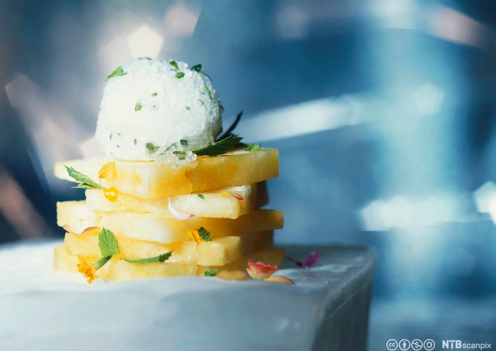 Skiver av bakt ananas servert med ei kule kokossorbé på toppen. Foto.