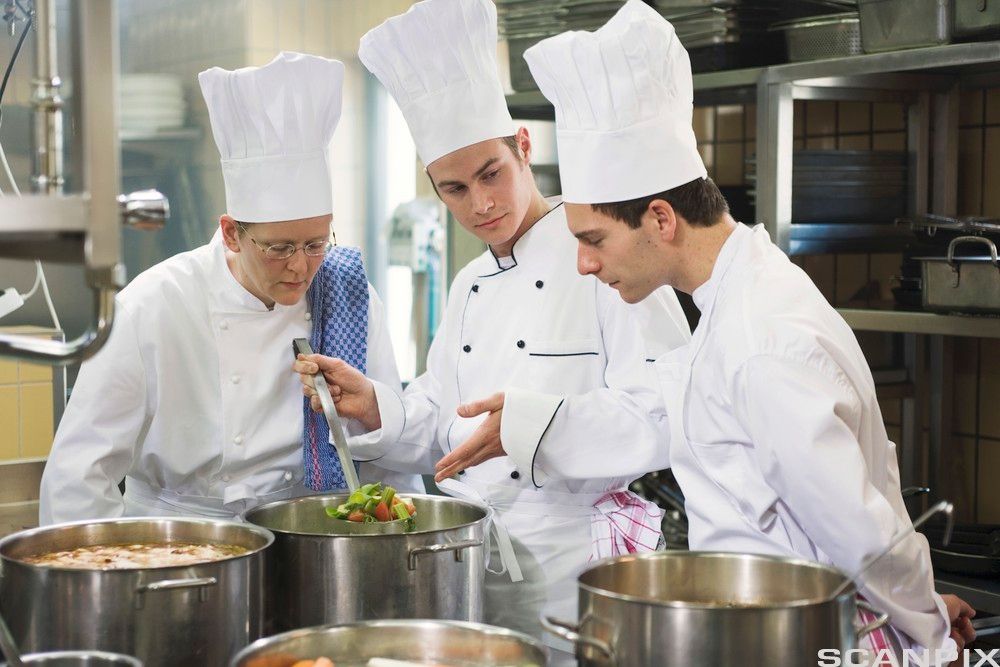 Tre kokker på et kjøkken står over gryter med kraft og diskuterer. Foto.