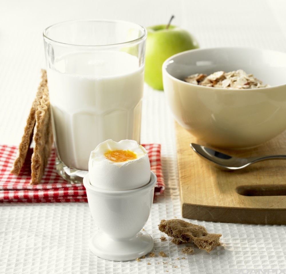 Foto av et måltid bestående av bløtkokt egg i et eggeglass, et glass melk, en bolle med frokostblanding, et par knekkebrød og et eple.