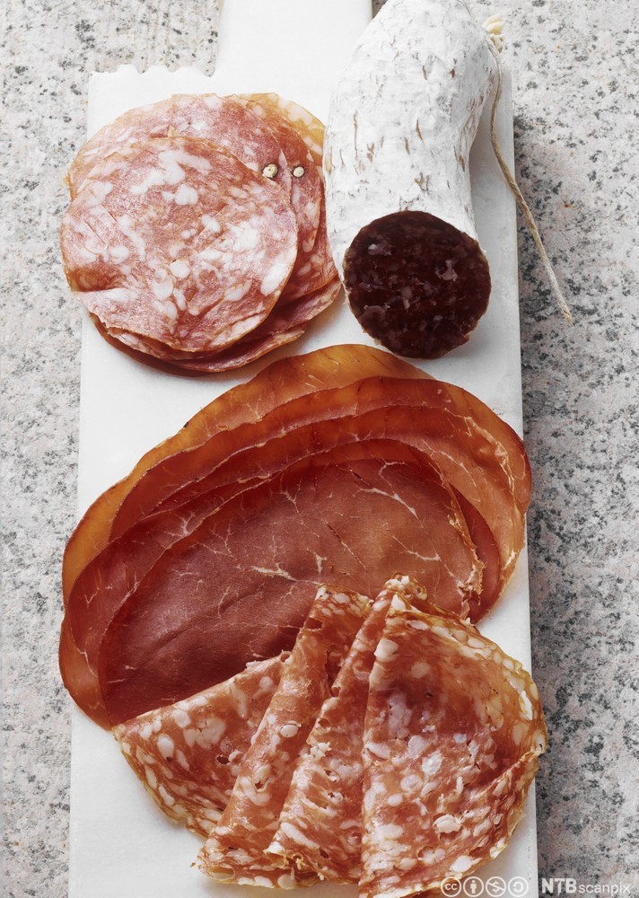 Fjøl med oppskoren spekemat som pølser og skinke. Foto.