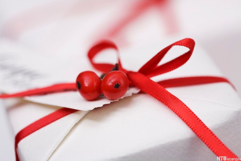 Gift wrapped in white paper with a red bow and two red berries. Photo.
