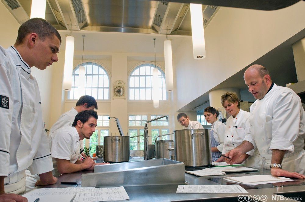 Kokker samlet rundt kjøkkenøy. De har planleggingsmøte. Foto.