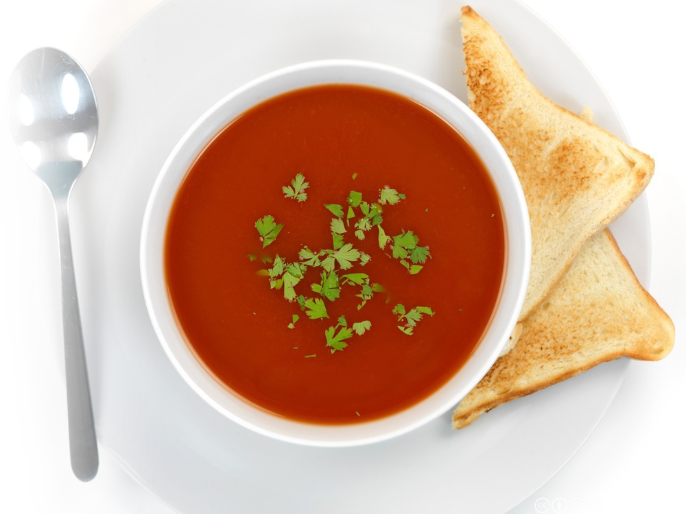 Tomatsuppe i ei skål med rista brødskiver ved siden av. Foto.