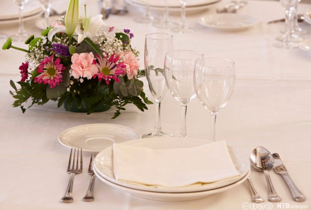En fint dekket kuvert på en restaurant med en rosa blomsteroppsats. Foto. 
