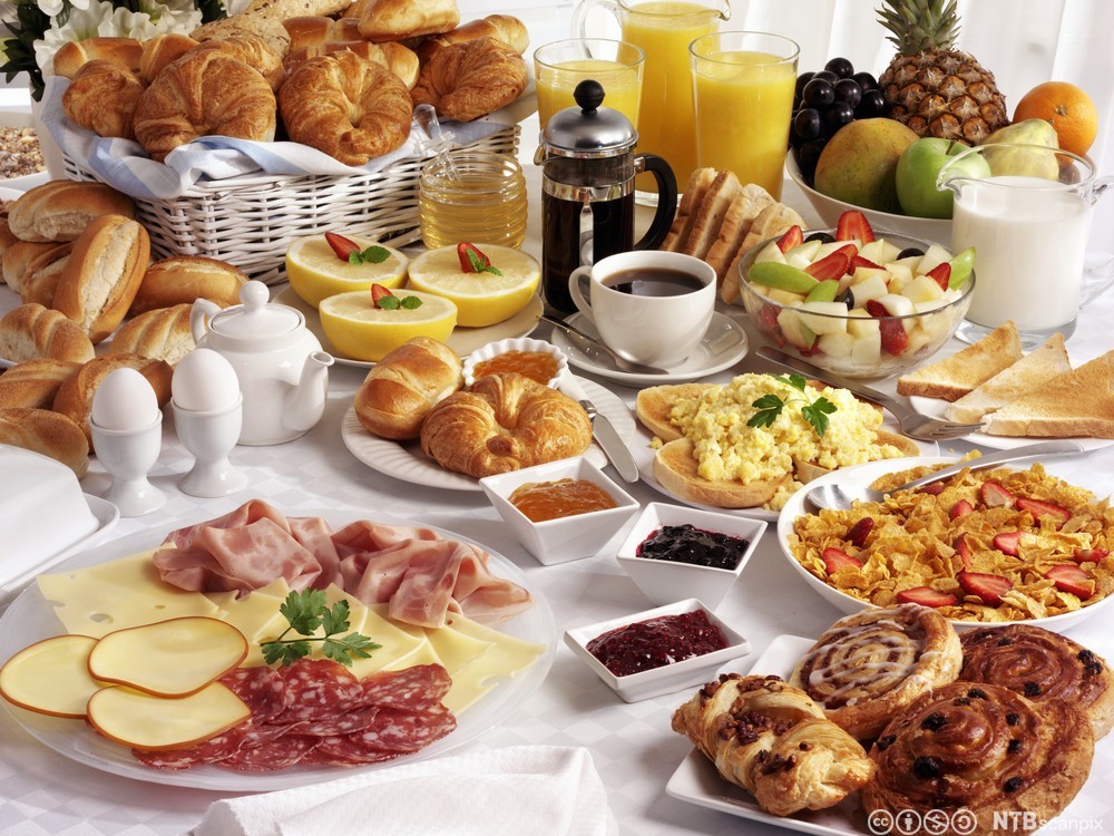 Et bugnende frokostbord med bakervarer, pålegg, frukt, drikke og anna. Foto.