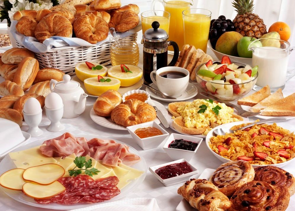 Et bugnende frokostbord med bakervarer, pålegg, frukt, drikke og anna. Foto.