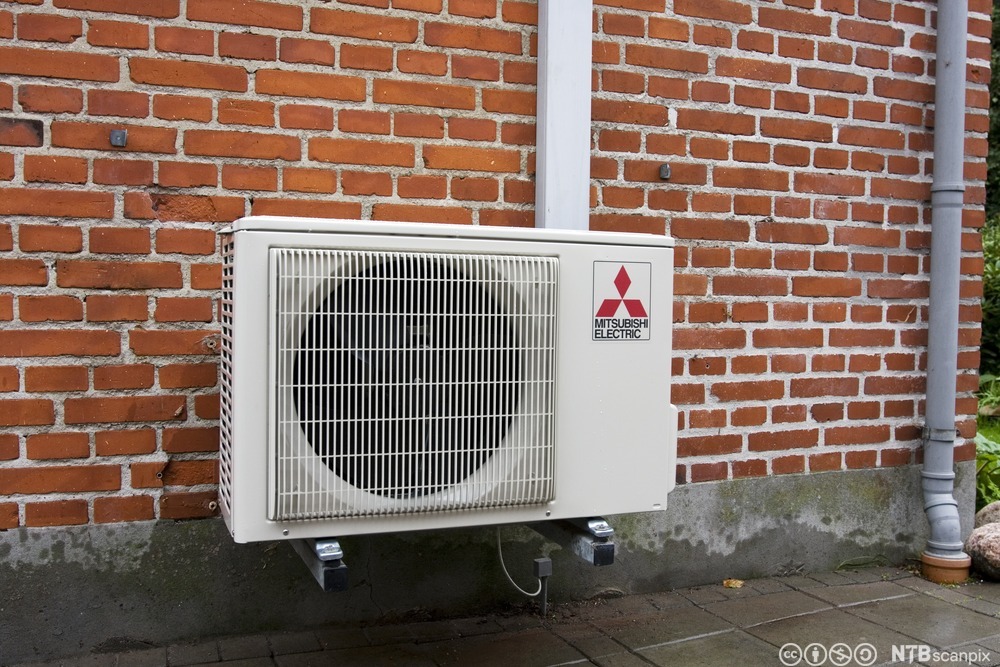 Bilde av Mitsubishi varmepumpe som er montert utvendig på en brun murvegg. Foto.