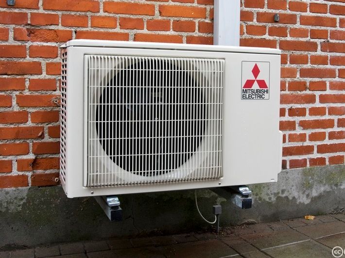 Bilde av Mitsubishi varmepumpe som er montert utvendig på en brun murvegg. Foto.