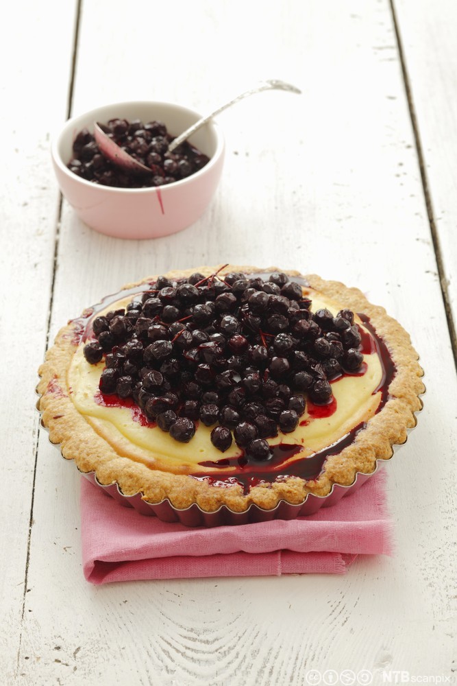 En terte fylt med vaniljekrem og en haug svarte bær. Foto.