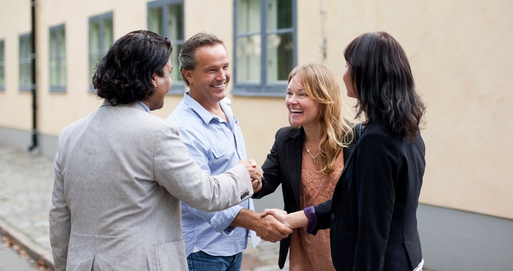 Fire vaksne helsar på kvarandre. Foto.