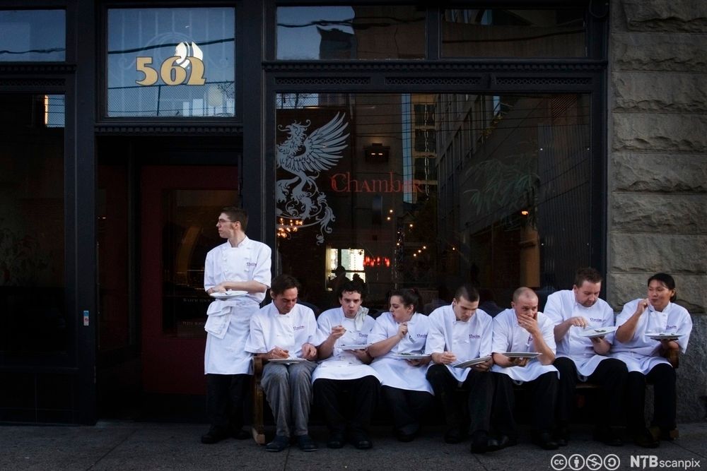 En rekke av kokker som sitter utenfor en restaurant og har spisepause. Foto.
