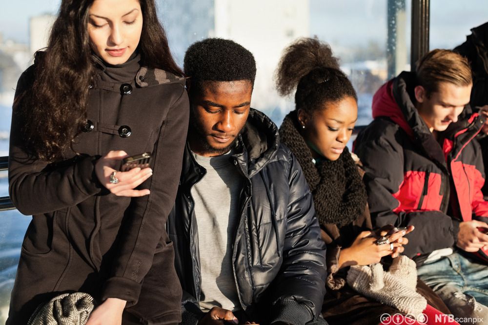 Fire ungdommer på en holdeplass er opptatt med hver sin mobiltelefon. Foto.