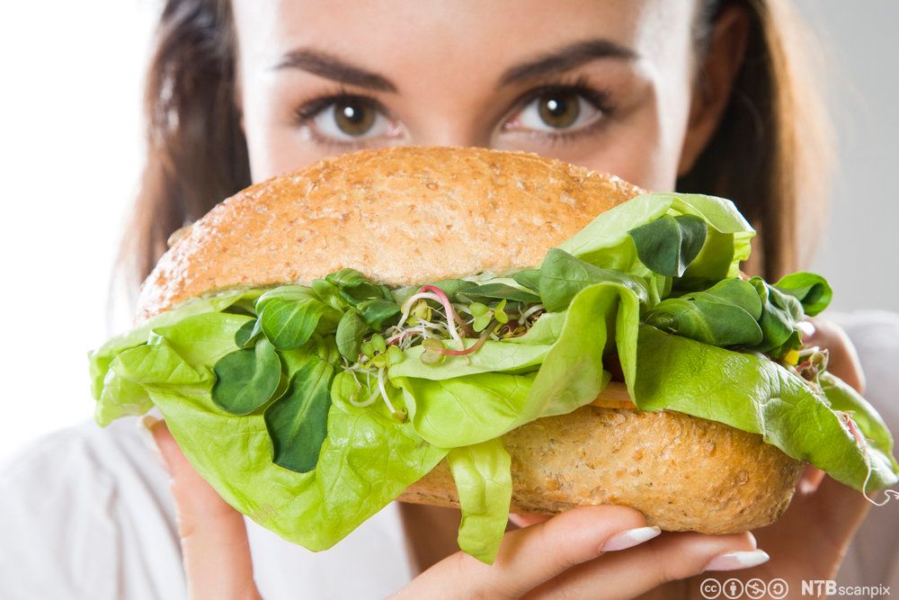 En kvinne holder fram et grovt bakverk fylt med salat. Foto.