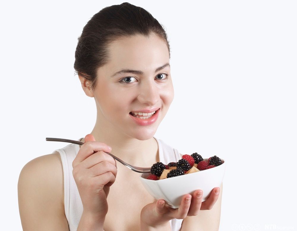 En ung dame spiser en dessert med bjørnebær, epler og bringebær. Foto.