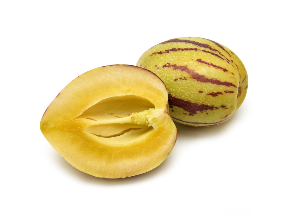 Ein hel og ein delt pepino frukt mot kvit bakgrunn. Foto.