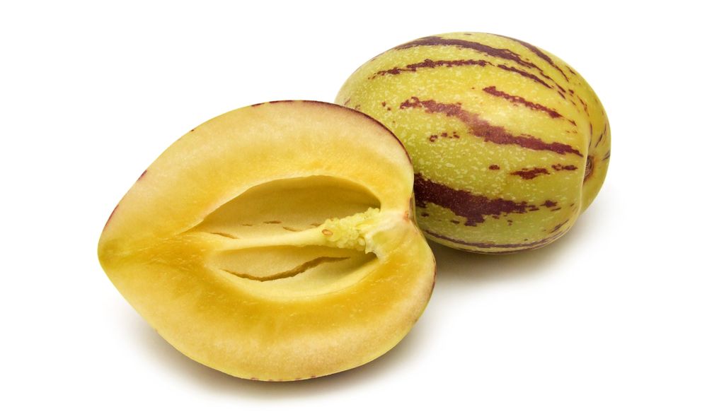 En hel og en delt pepino frukt mot hvit bakgrunn. Foto.
