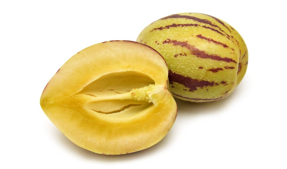 Ein hel og ein delt pepino frukt mot kvit bakgrunn. Foto.