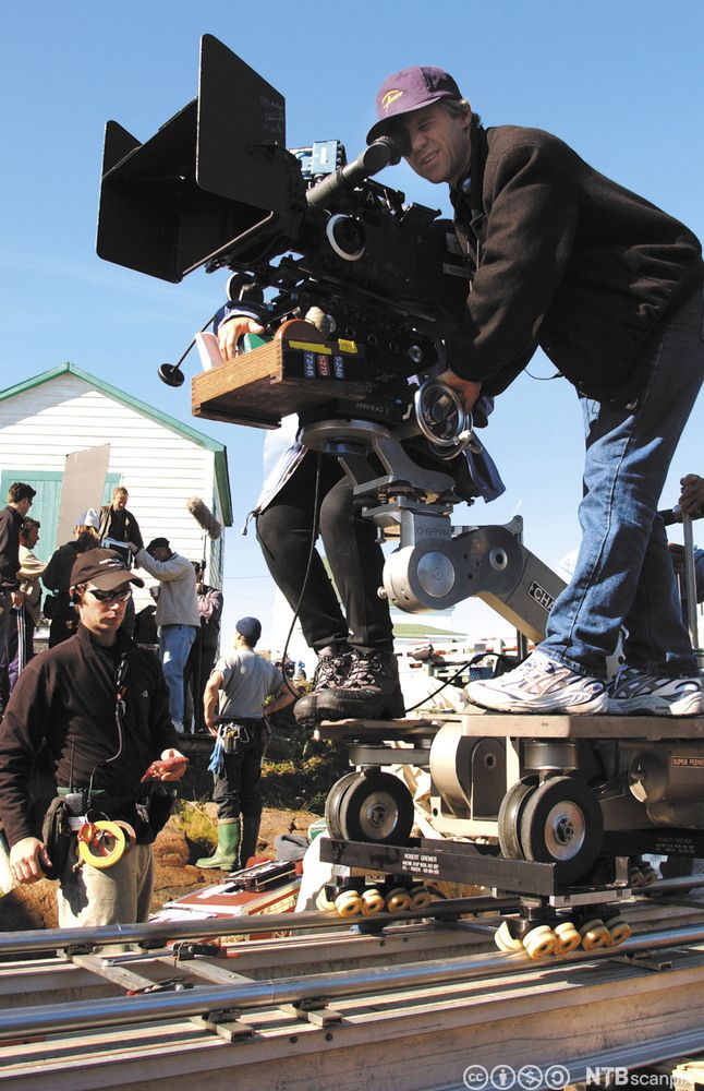 Ein mann køyrer filmkamera på skjener. Foto.