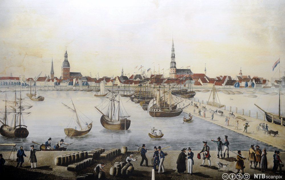 Havna i Riga på 1700-tallet. Skip i havna. Mennesker og tønner i forkant. Bebyggelse med flere kirker i bakgrunnen. Trykk.