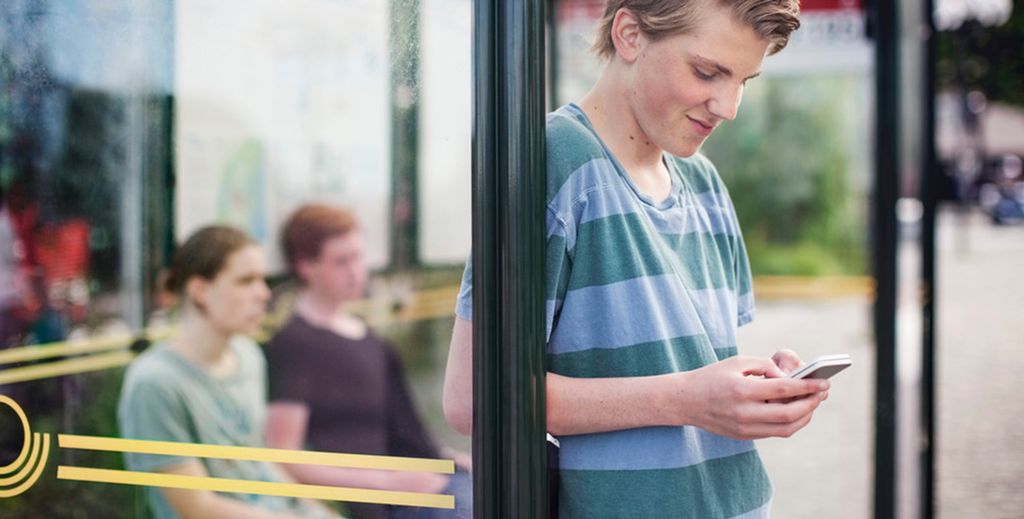 Tre ungdommer venter på t-banen. En ser ned på mobilen. Foto.