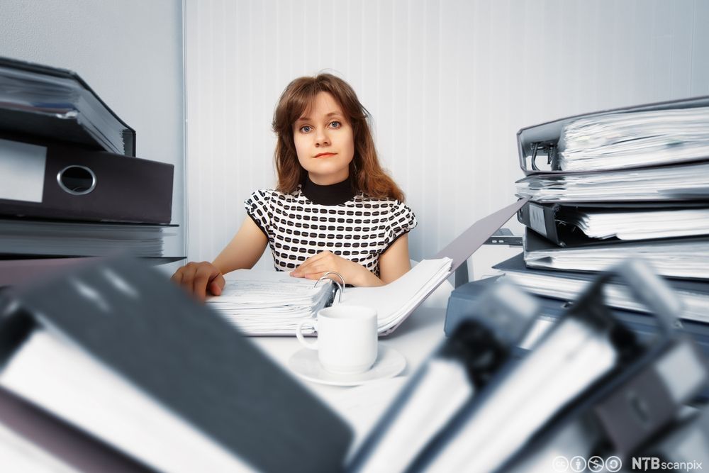 Regnskapsfører med mange permer på kontoret. Foto.