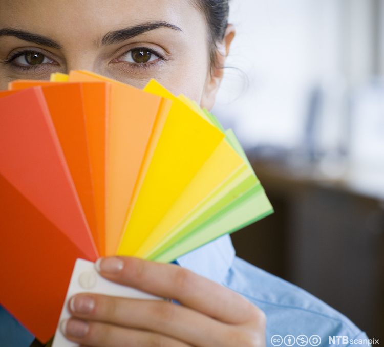 Kvinne med fargekart foran ansiktet. Foto