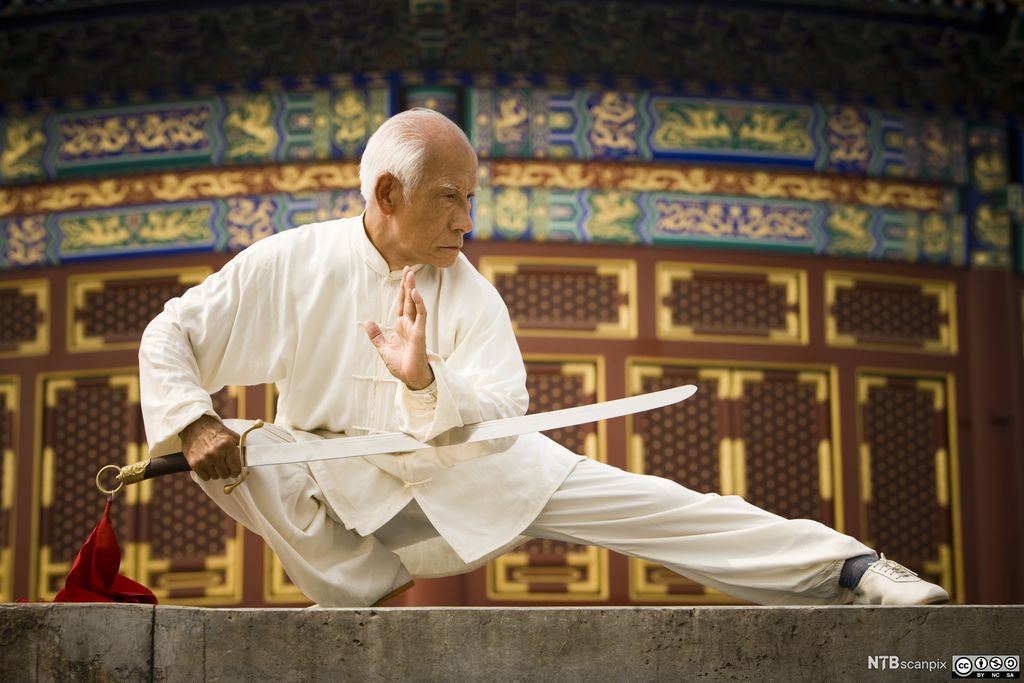 Eldre kinesisk mann trener Kung Fu med sverd. Foto.