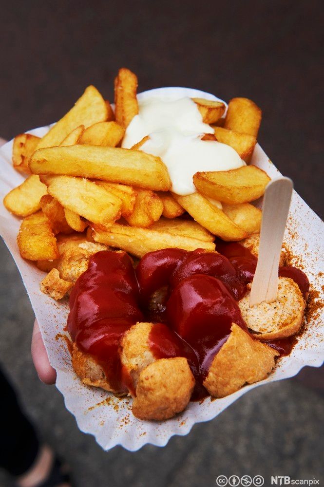 Currywurst, som består av tysk pølse med pommes frites. På toppen er det ketsjup og majones. Foto.
