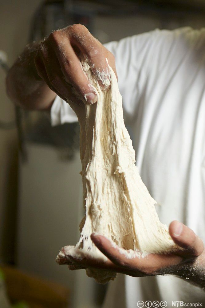 En baker som strekker ut en deig med mye gluten. Foto.