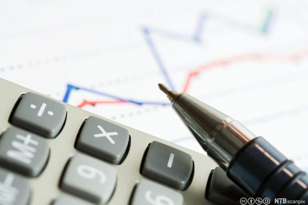 Nærbilde av en del av en kalkulator og tuppen av en kulepenn. I bakgrunnen er det en graf. Foto.