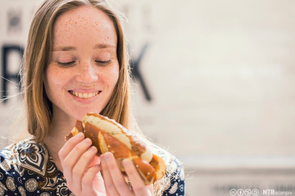 Ung kvinne et pølse i brød. Foto.