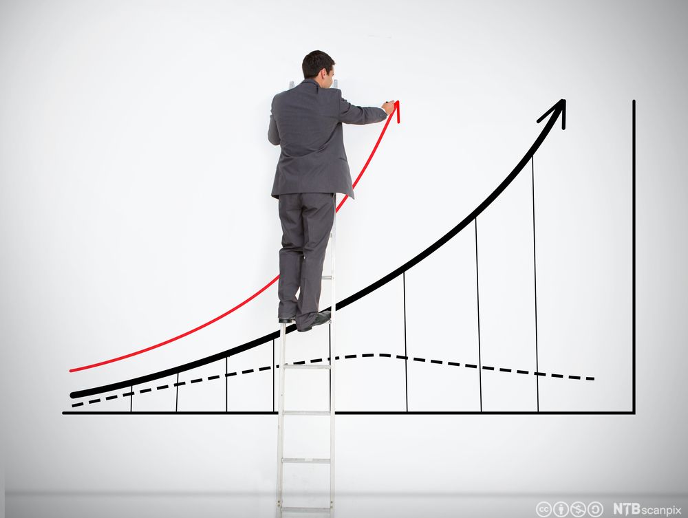 Mann står på en stige og tegner en graf på en hvit vegg. Foto.