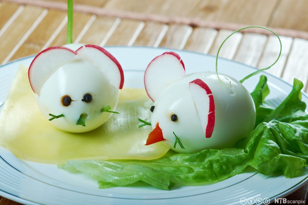To egg som er dekorerte med peparkorn og diverse grønsaker slik at dei ser ut som mus. To reddikskiver som er stukne inn i kvart egg, tener som øyre. Foto.