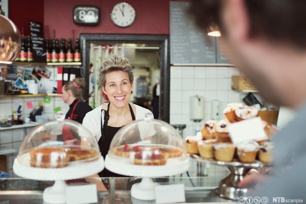 En smilende servitør bak en kafédisk. Foto.