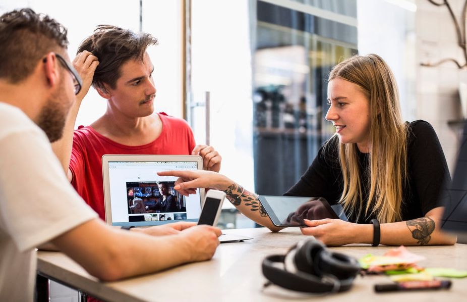 Tre personer diskuterer et bilde på en PC-skjerm. Foto.