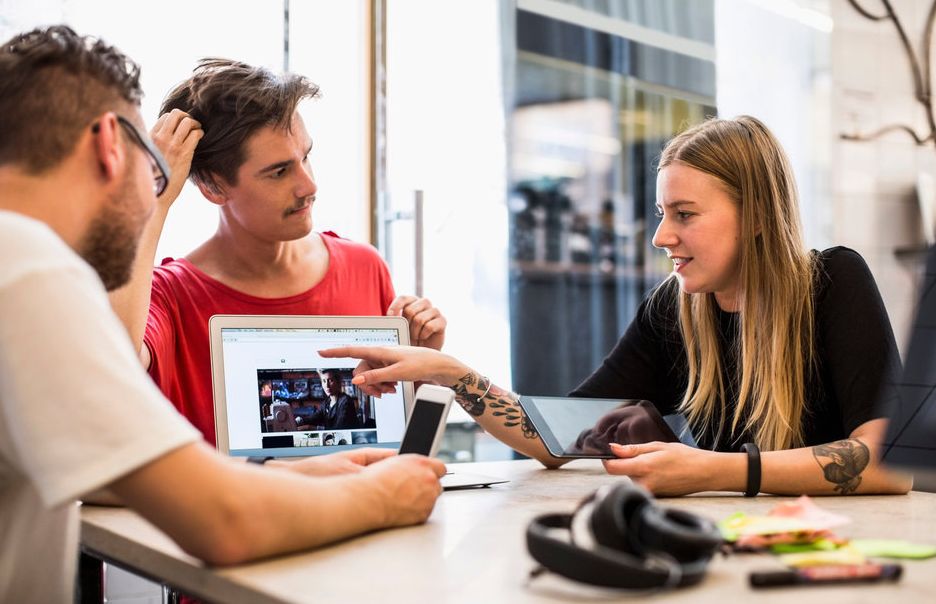 Tre personar diskuterer eit bilete på ein PC-skjerm. Foto.