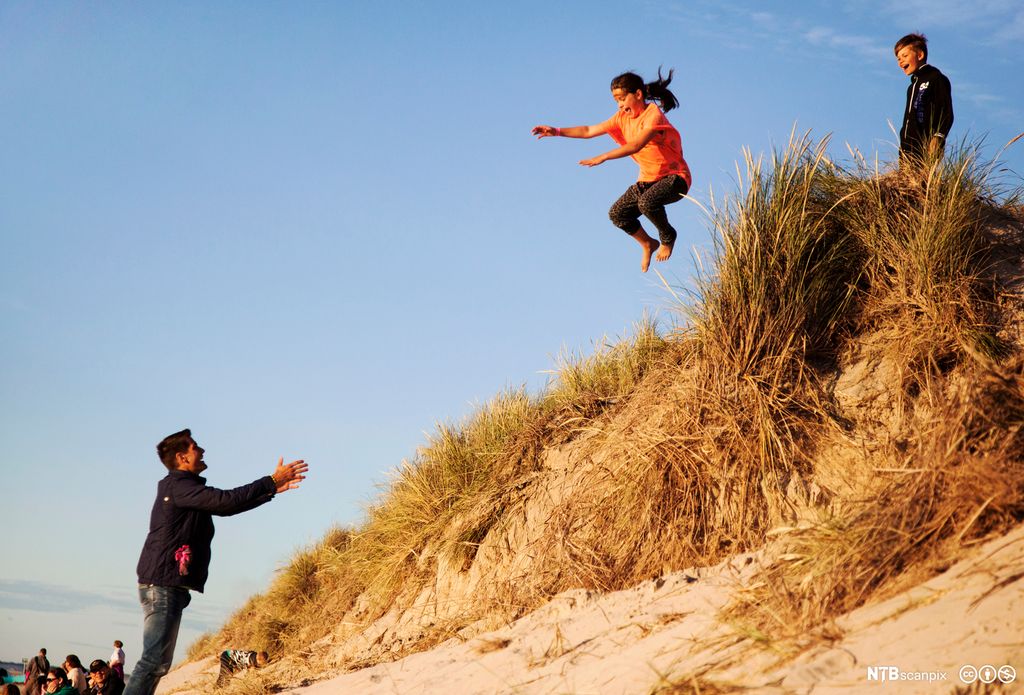 Jente som hopper fra en kant og en mann tar imot. Foto.