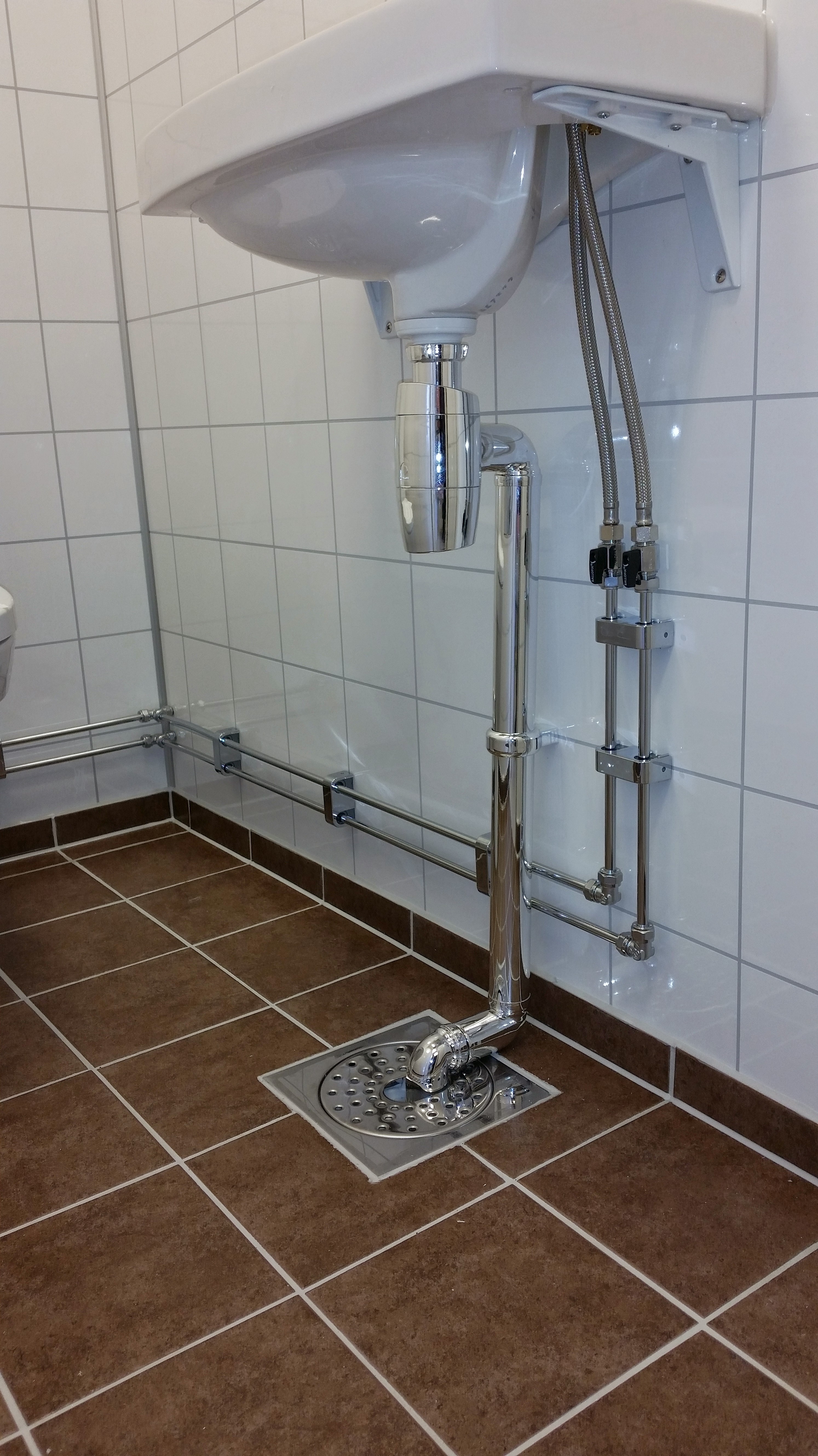 Servantrør som fører ned i sluket på et flislagt våtrom. Foto.