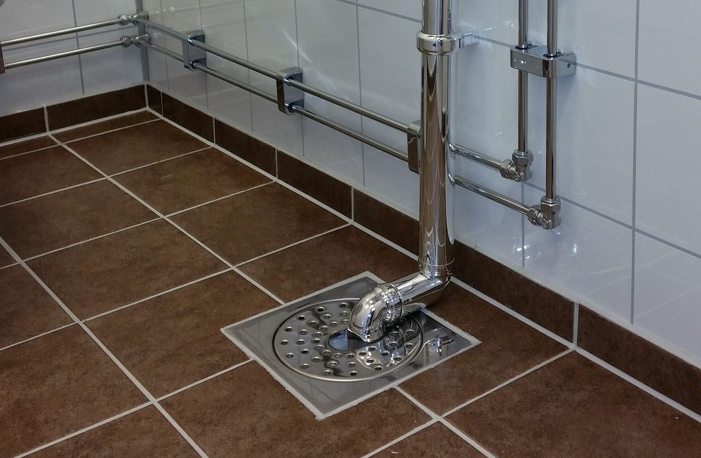 Servantrør som fører ned i sluket på et flislagt våtrom. Foto.