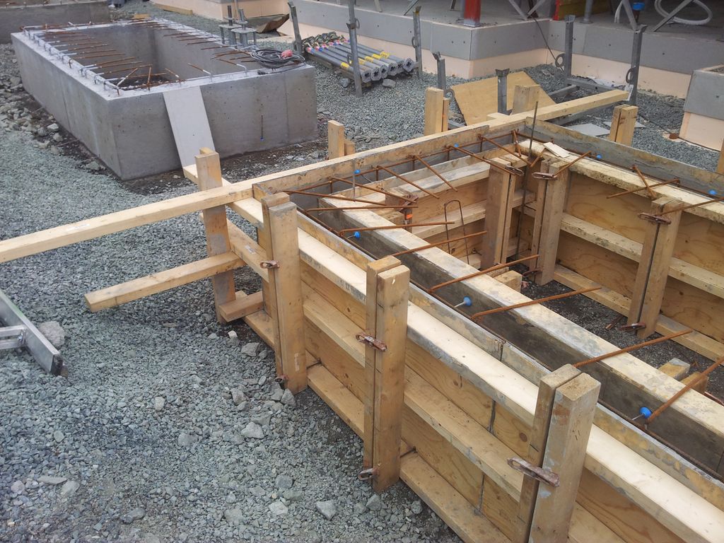 Forskaling for ringmur med armering stikkande opp. Ved sida av ser vi ein ferdig ringmur. Foto.