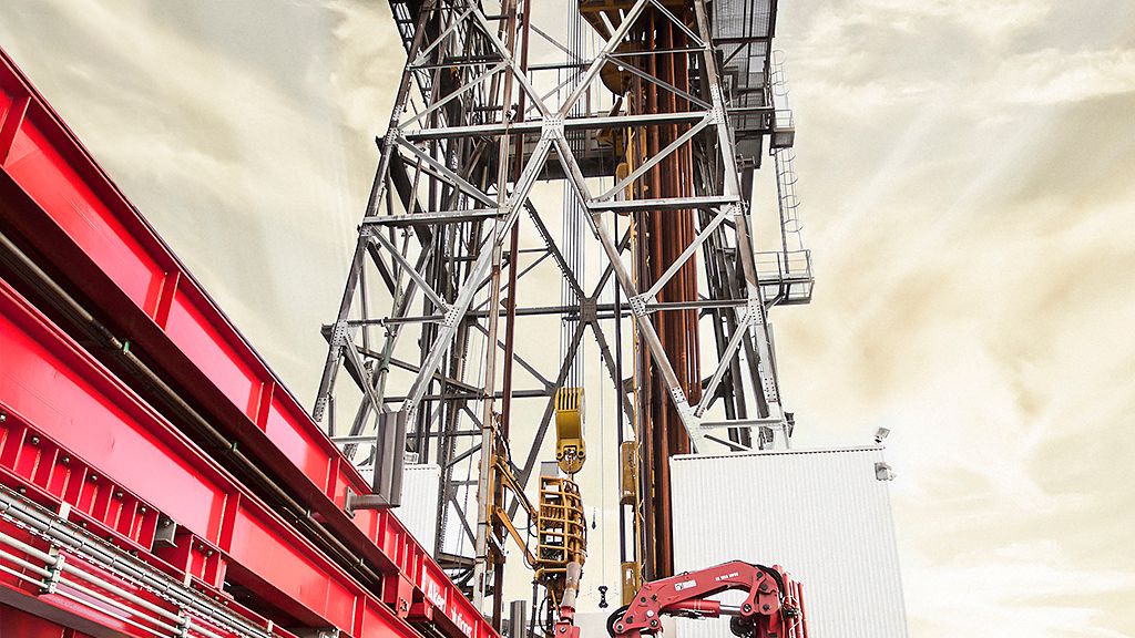 Boretårn med rød bro og solrik himmel med lett skydekke i bakgrunnen. Foto.