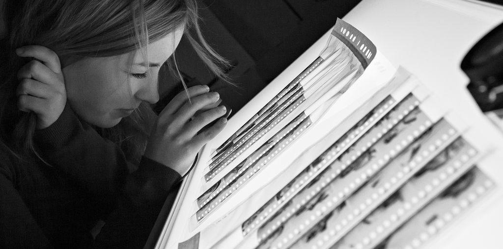 Kvinne undersøker negativer som ligger på et lysbord med lupe. Foto.