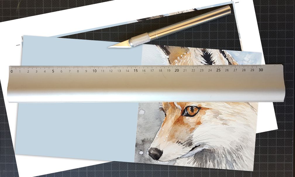 Utskrift av et kort på ei skjærematte sammen med en papirkniv og en linjal i metall. Foto.