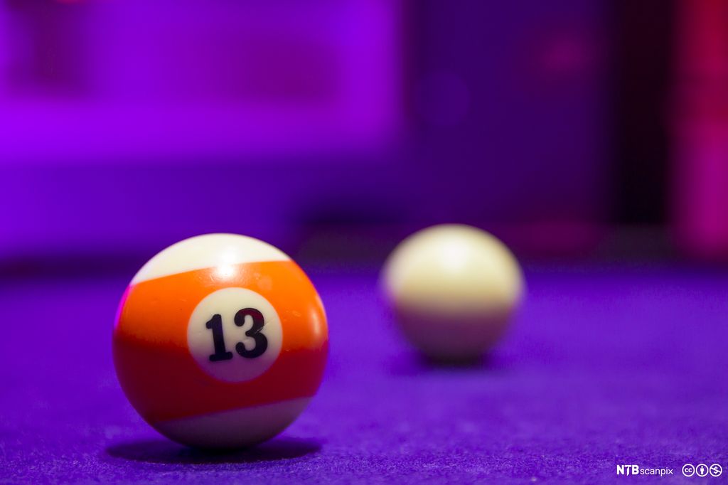 Billiardkuler på et bord. Orange kule nummer 13 i forgrunnen. Hvit kule i bakgrunnen. Foto.