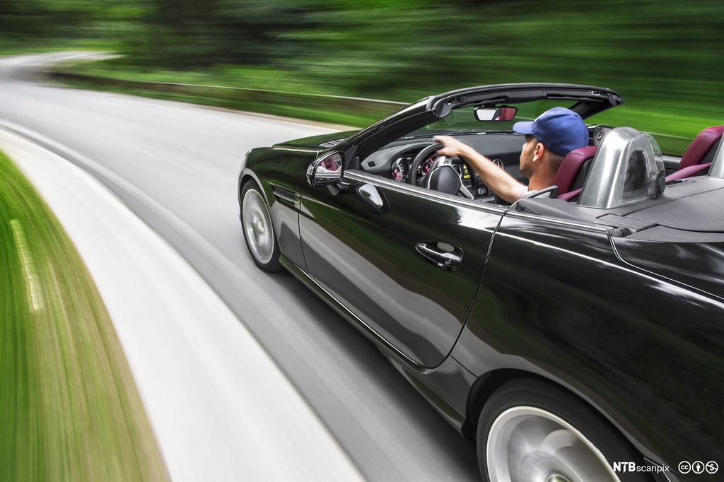 Mann i sort sportsbil kjører fort. Foto.