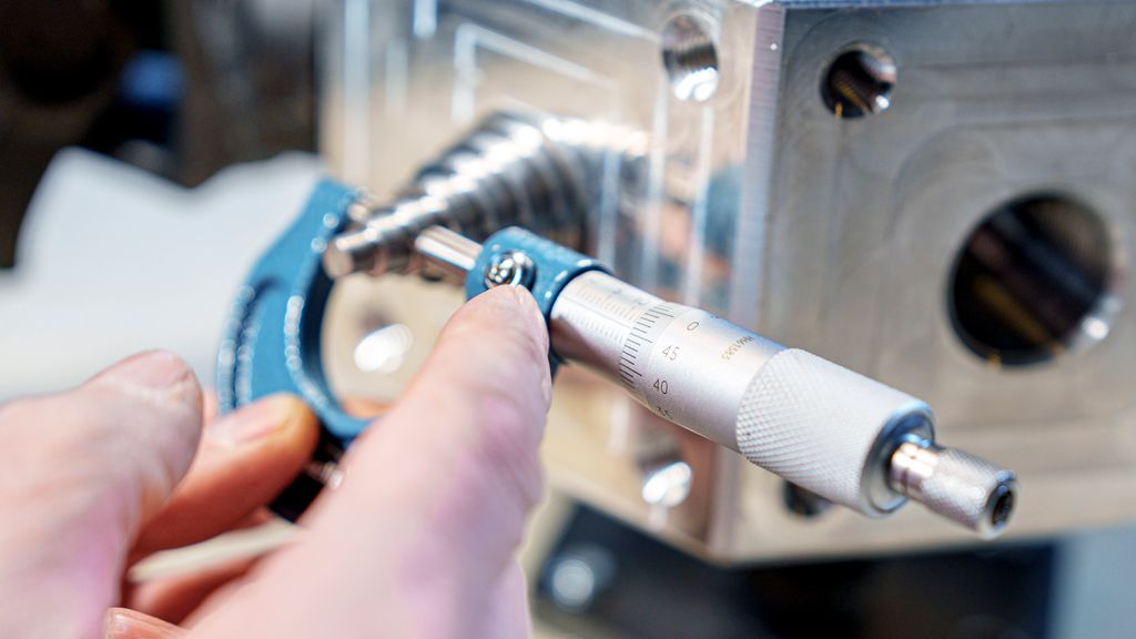 En person låser låseskruen på et mikrometer. Foto.
